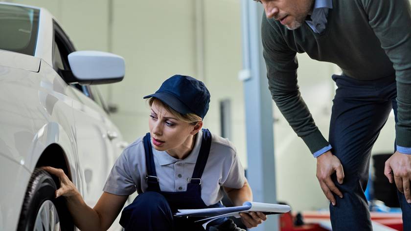 Female mechanic inspecting a car tire while discussing maintenance details with a customer inside an auto repair shop.