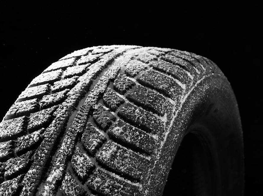 Close-up of a winter tire covered in snow, showing deep tread patterns designed for traction on icy roads.